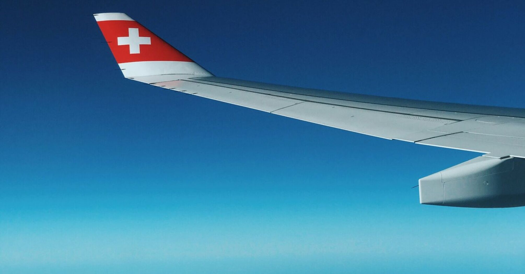 View of airplane wing with Swiss flag flying above the clouds and mountains