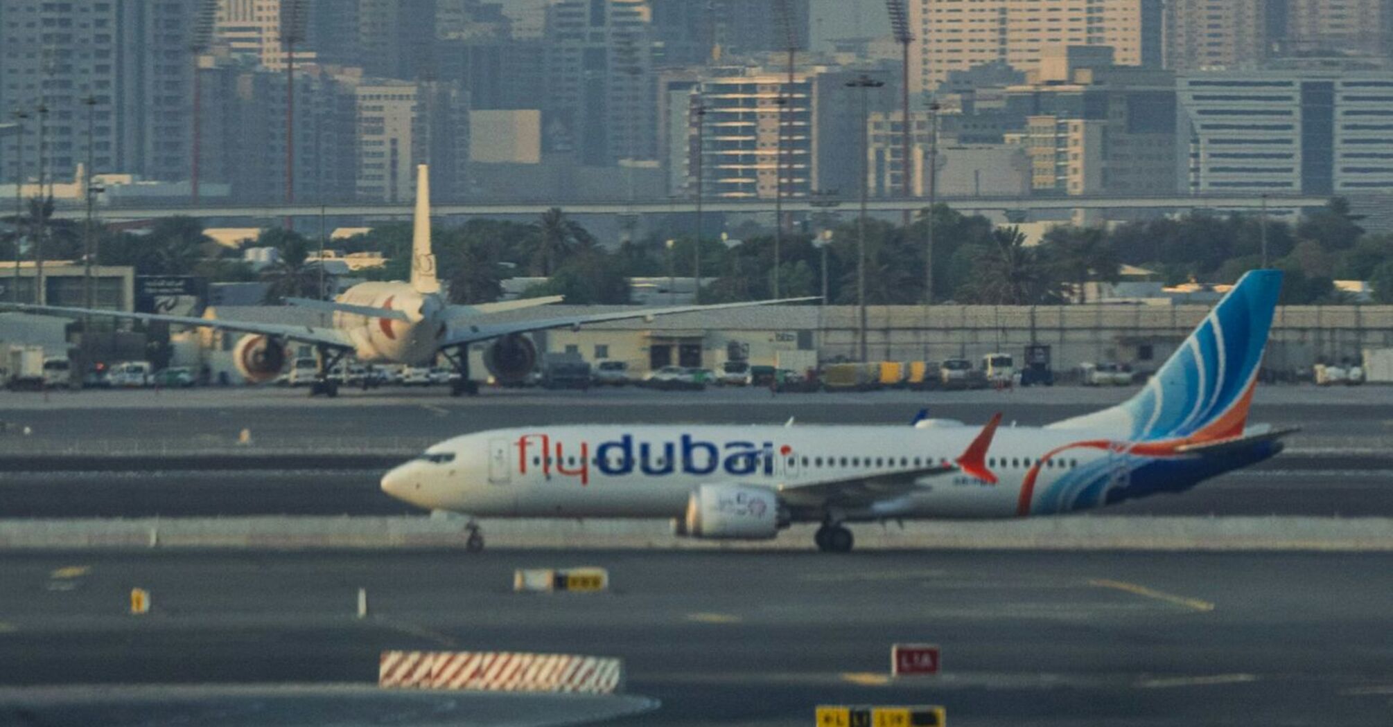 A Flydubai airplane on the runway at Dubai International Airport with a cityscape in the background