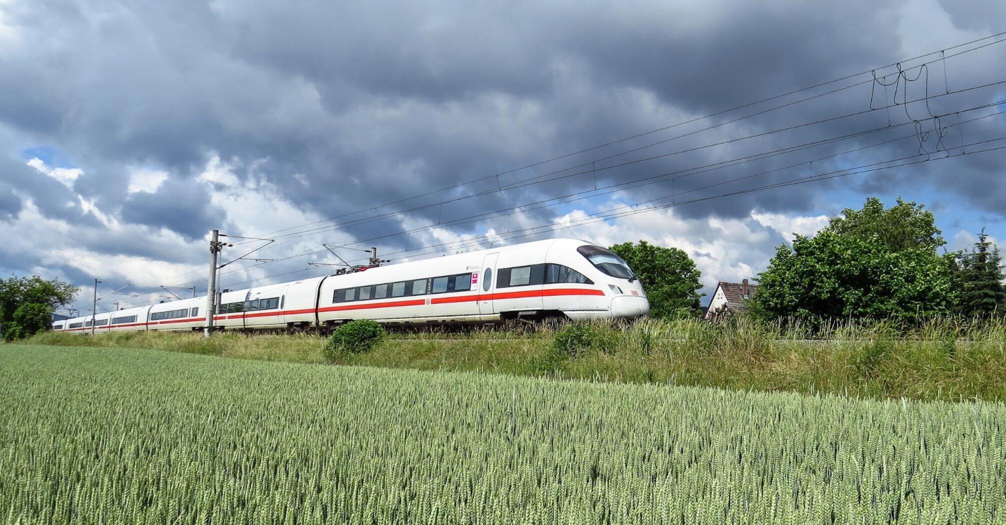 High-speed train moving through a lush green field under a cloudy sky