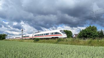 High-speed train moving through a lush green field under a cloudy sky