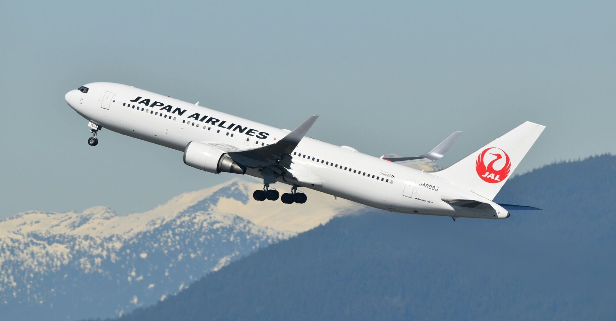 A Japan Airlines plane takes off against a backdrop of snow-covered mountains