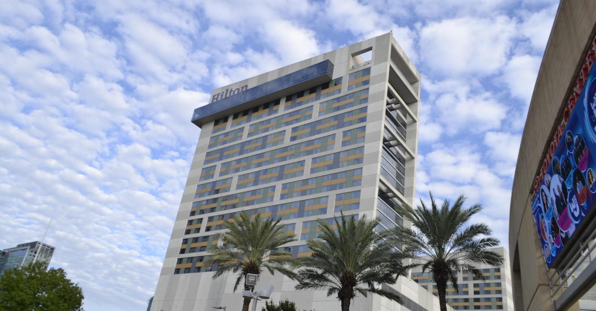 Hilton hotel building under a partly cloudy sky flanked by palm trees