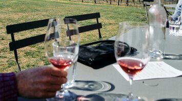 A picturesque vineyard nestled between mountain ranges, with wine glasses on a table in the foreground, hinting at a wine tasting experience