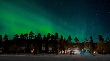 Northern lights illuminating the sky over a snowy forest with cabins below