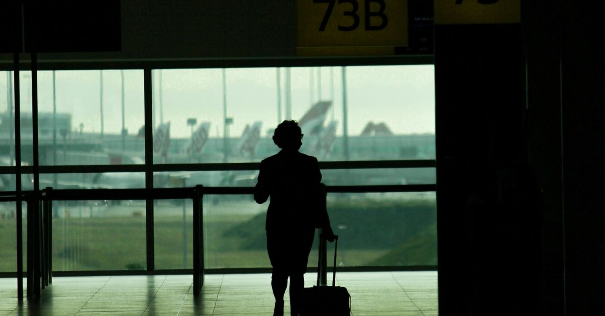 Silhouette of a traveler pulling luggage through a Brisbane airport terminal near gates 73 and 74