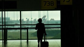 Silhouette of a traveler pulling luggage through a Brisbane airport terminal near gates 73 and 74
