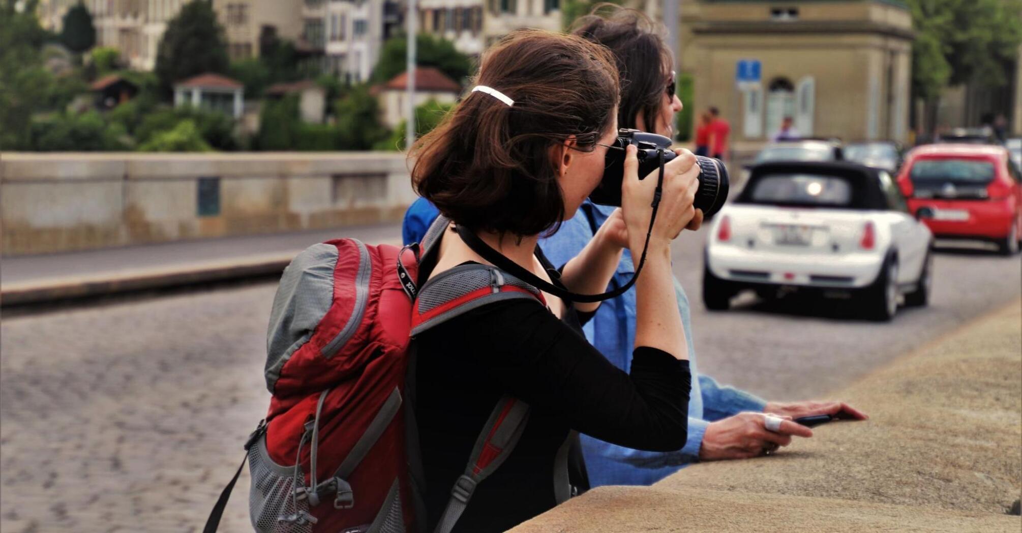 A tourist with a backpack takes photos of city views while standing on a bridge