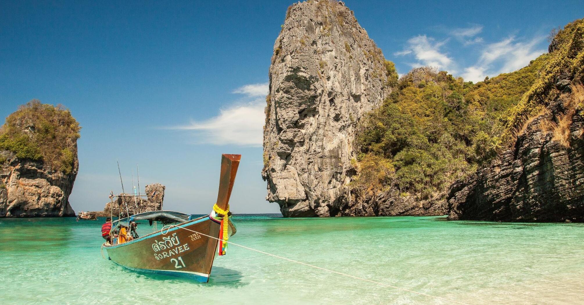 Traditional Thai longtail boat anchored in crystal-clear turquoise waters near a rocky cliff