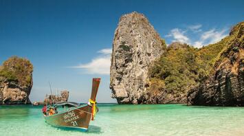 Traditional Thai longtail boat anchored in crystal-clear turquoise waters near a rocky cliff