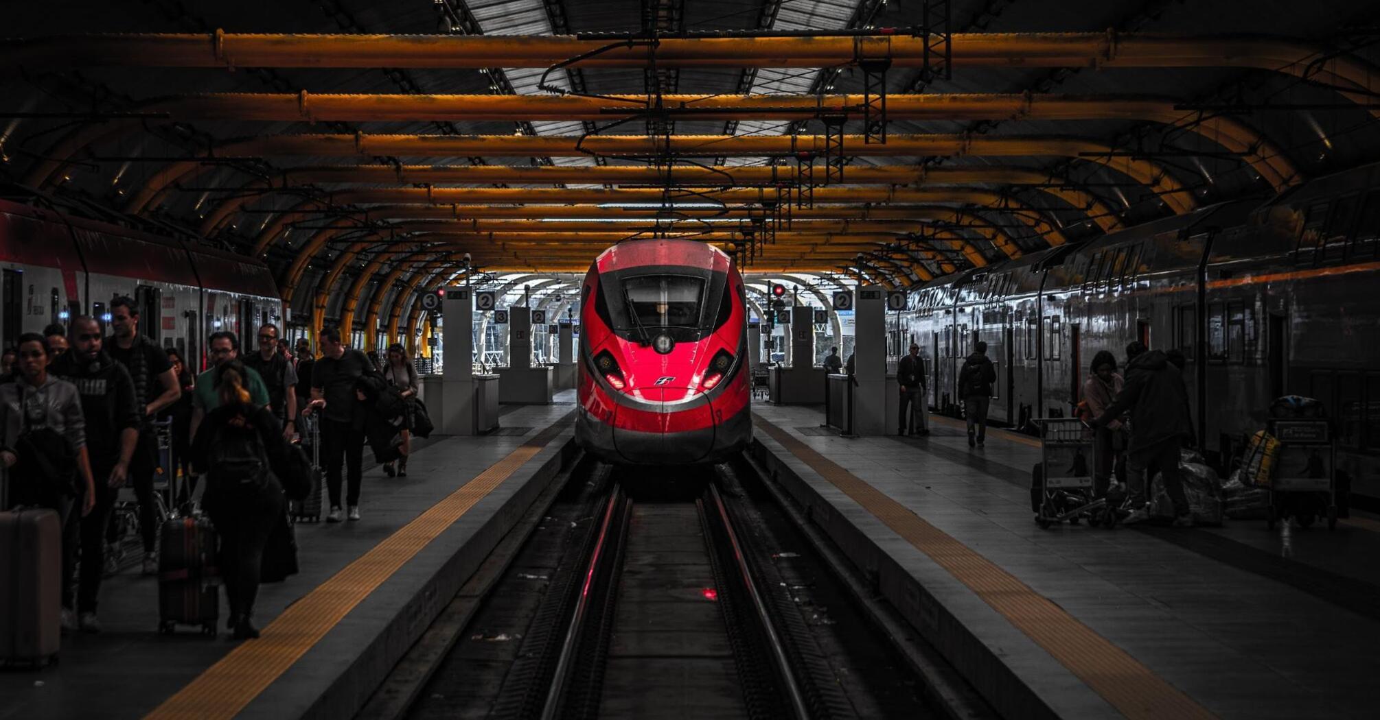 Red high-speed train at a station platform with passengers and luggage, under a curved yellow canopy