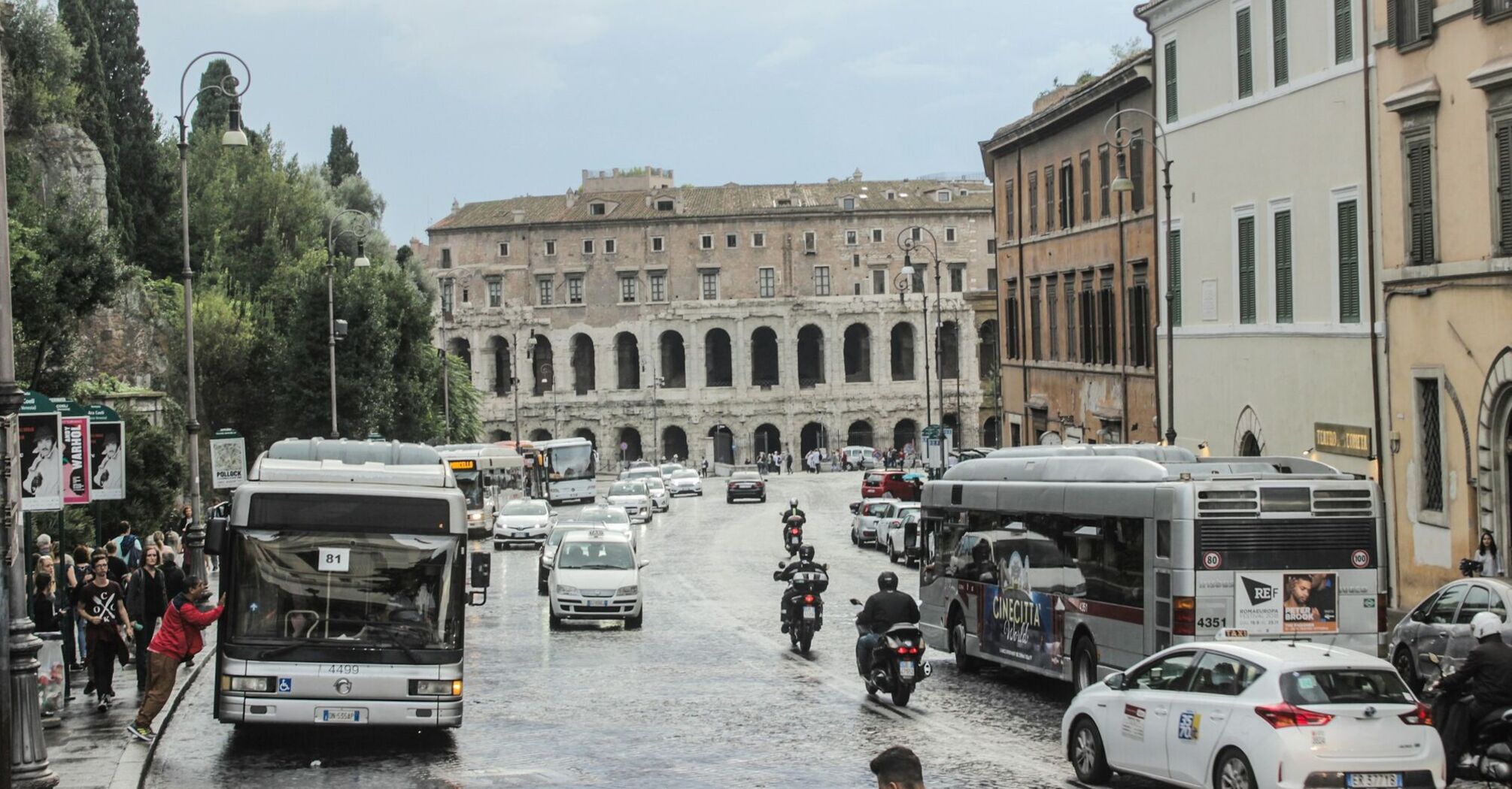 A street in Rome with public buses and motorbikes near historic buildings, showing local transportation in use