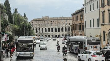 A street in Rome with public buses and motorbikes near historic buildings, showing local transportation in use