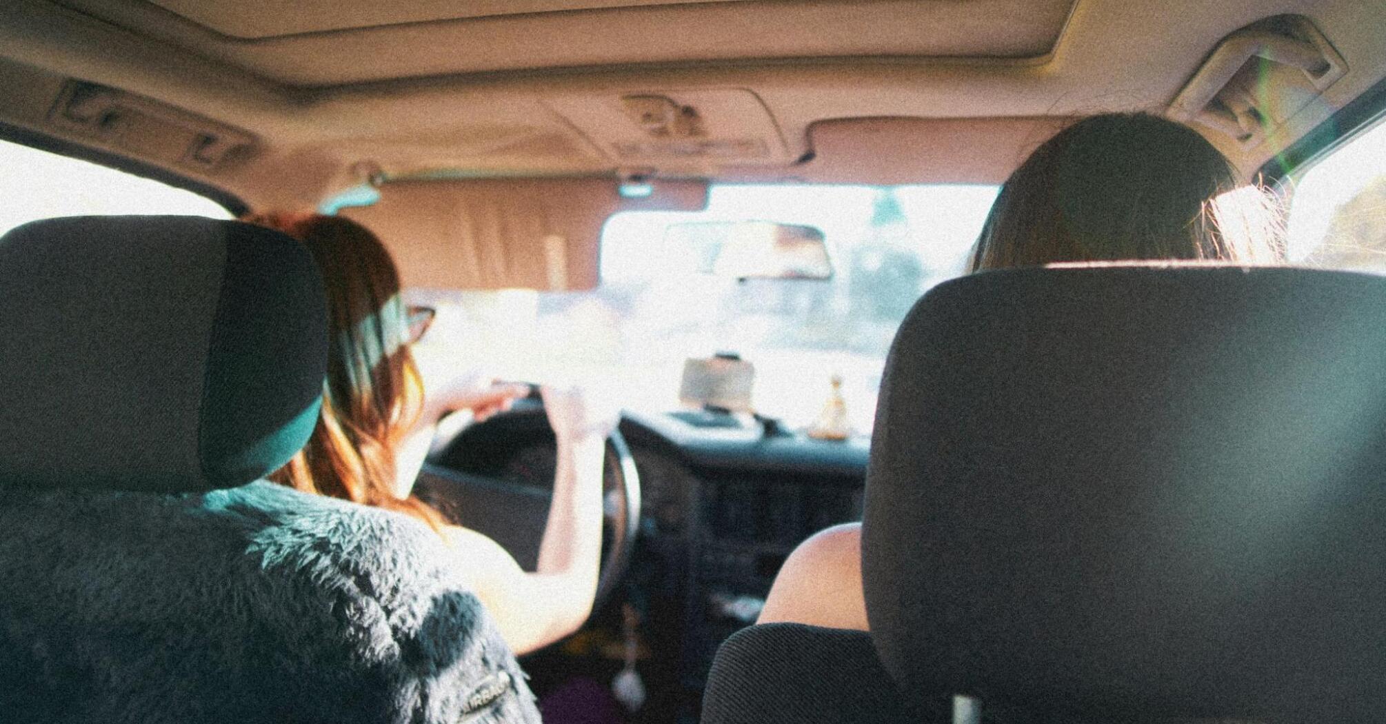 Two people driving in a car with a view from the backseat