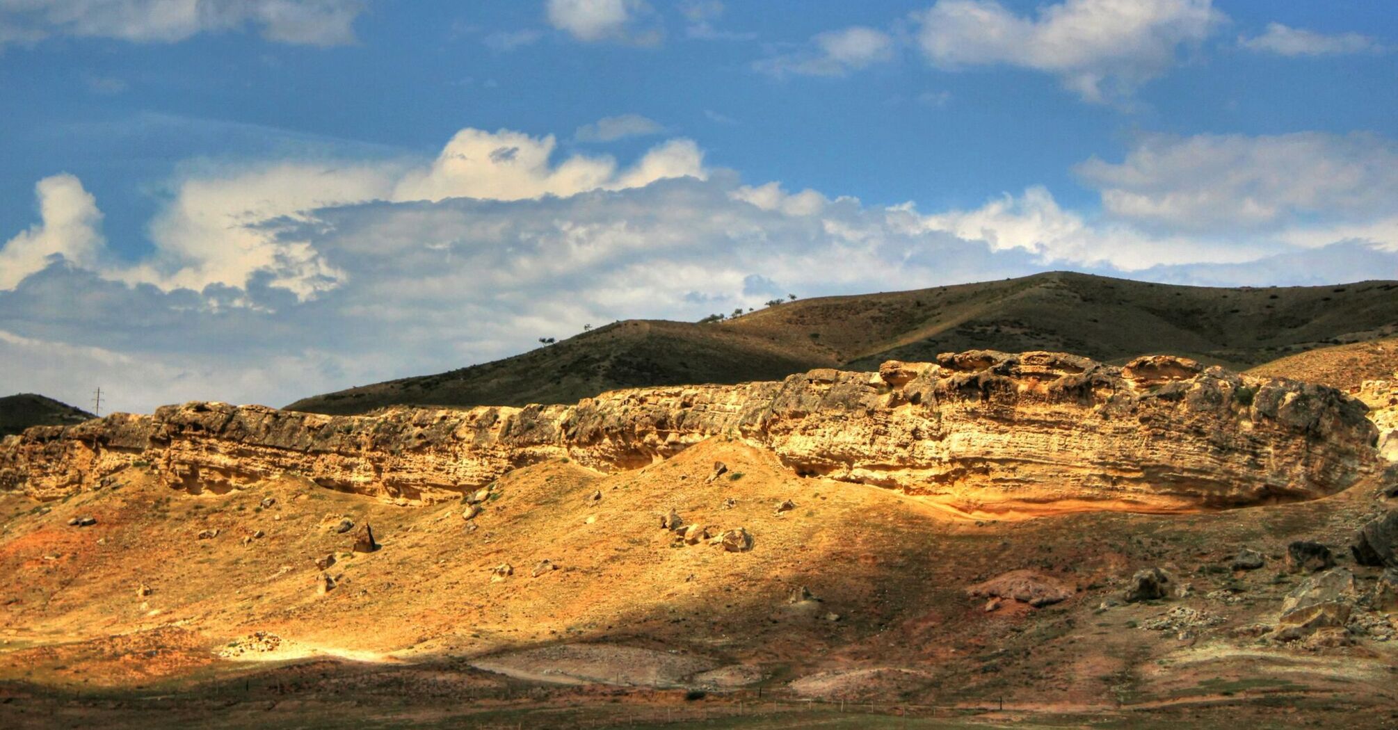 Sunlit rocky landscape under a blue sky with scattered clouds in Namangan region