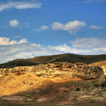 Sunlit rocky landscape under a blue sky with scattered clouds in Namangan region