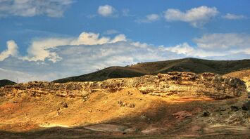 Sunlit rocky landscape under a blue sky with scattered clouds in Namangan region