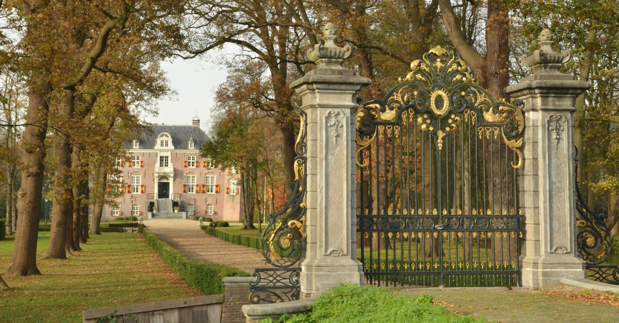 Ornate golden gates leading to a historic mansion surrounded by autumn trees