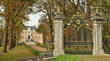 Ornate golden gates leading to a historic mansion surrounded by autumn trees