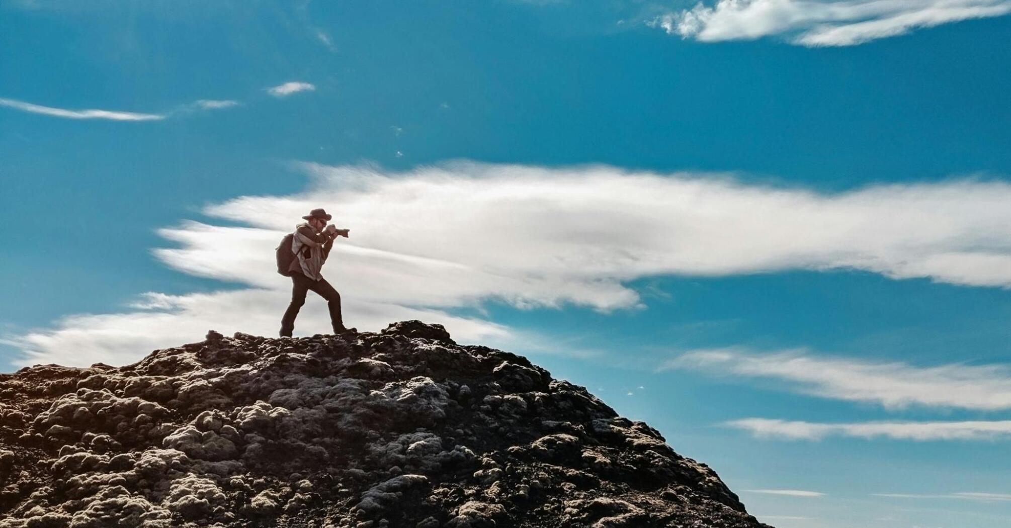 A photographer standing on a rocky hill under a clear blue sky