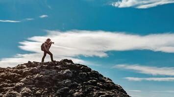 A photographer standing on a rocky hill under a clear blue sky