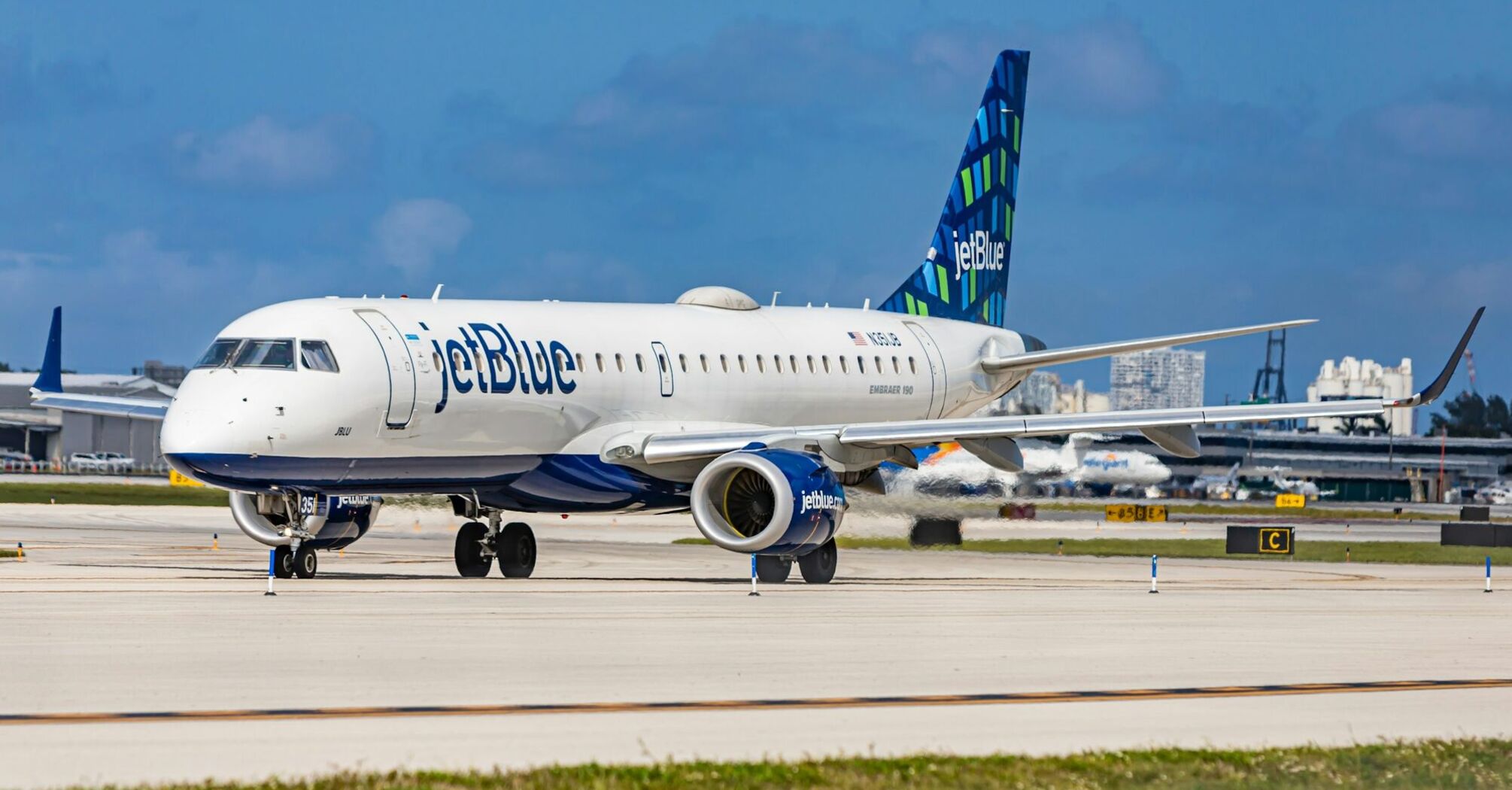 A JetBlue airplane taxiing on the runway at an airport with clear skies in the background