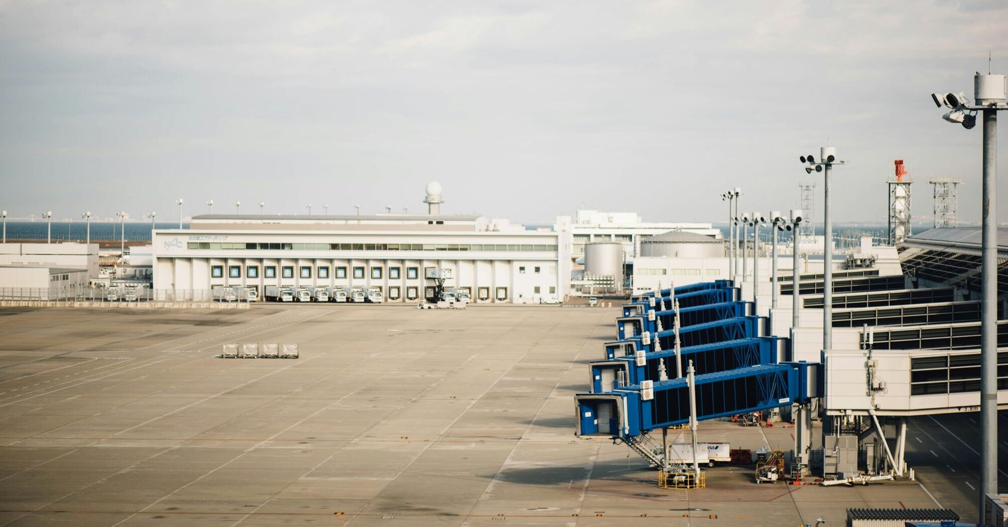 Empty airport tarmac with jet bridges and terminal building in the background under cloudy skies