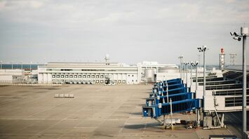 Empty airport tarmac with jet bridges and terminal building in the background under cloudy skies