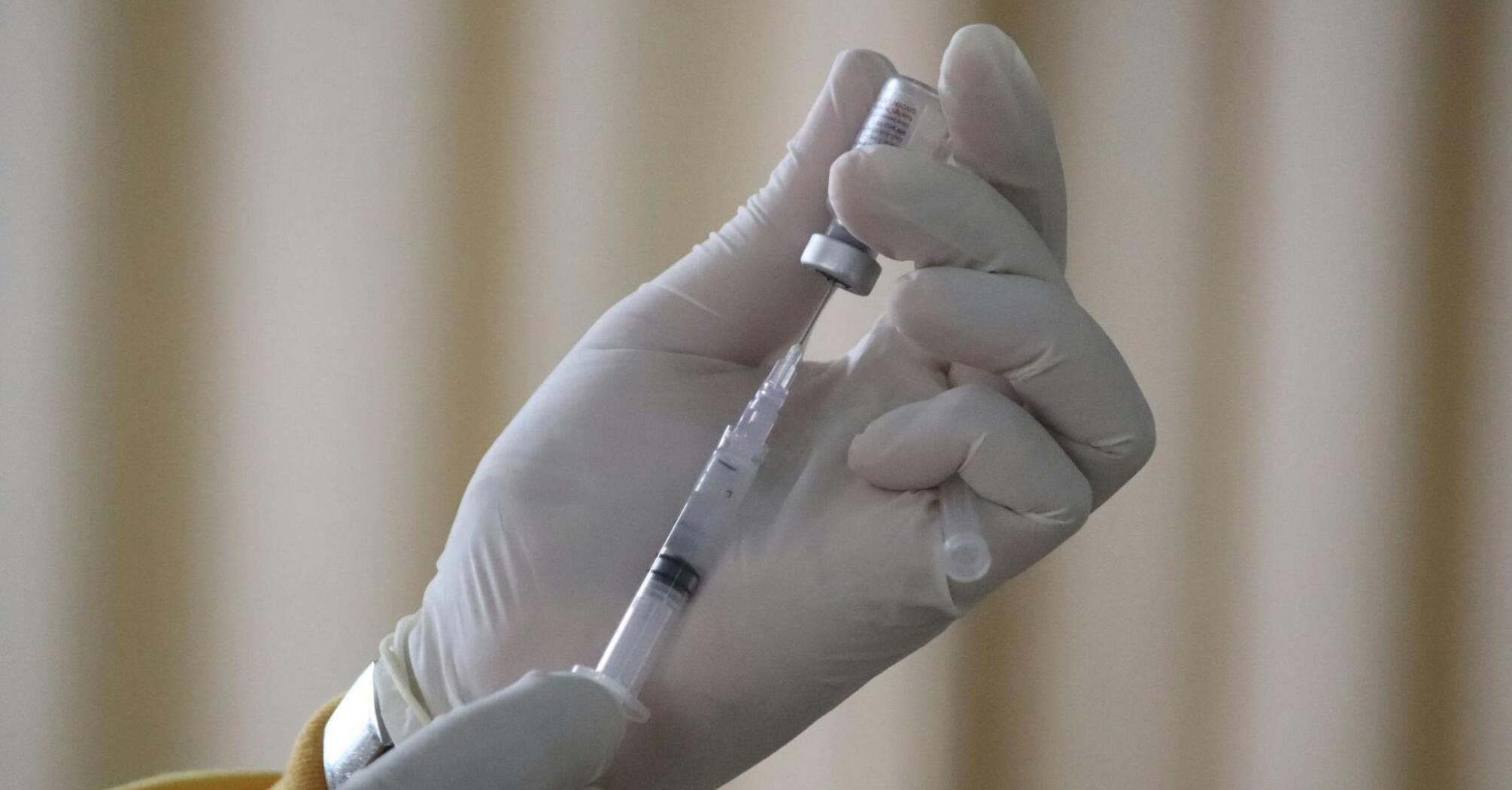 A gloved hand holding a syringe filled with a vaccine