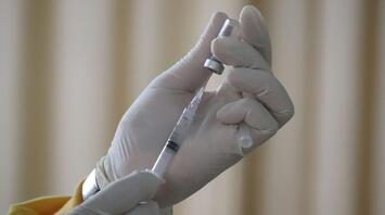 A gloved hand holding a syringe filled with a vaccine