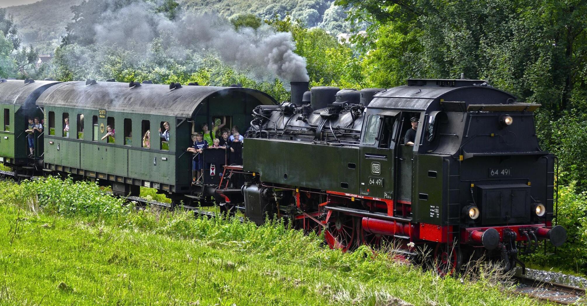 Vintage steam locomotive with passengers riding through lush greenery