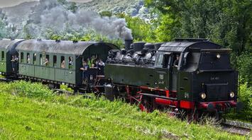Vintage steam locomotive with passengers riding through lush greenery