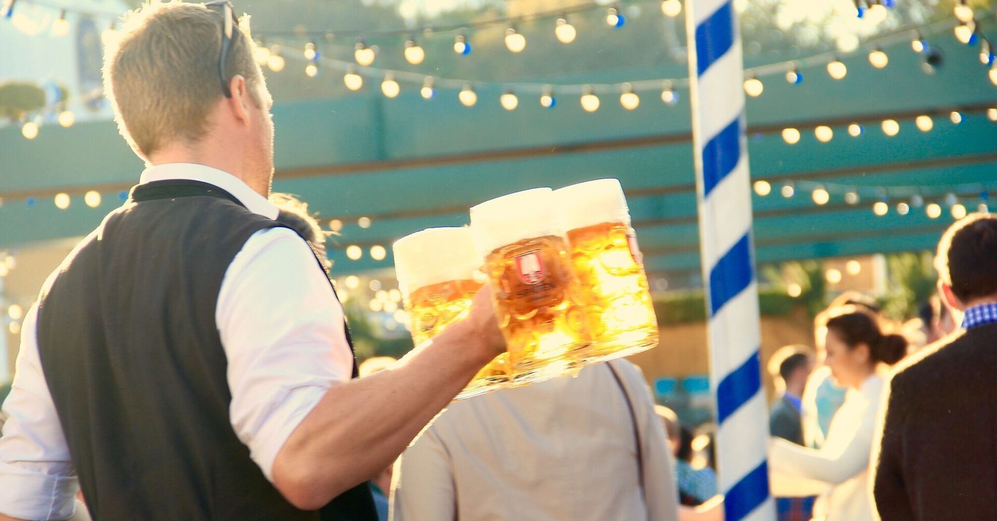 A server at Oktoberfest carrying multiple beer steins in a festive outdoor setting