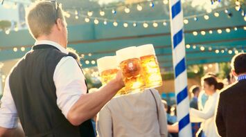 A server at Oktoberfest carrying multiple beer steins in a festive outdoor setting