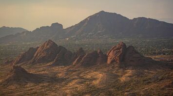 A scenic view of a desert landscape with rocky formations in the foreground and mountains in the background under a cloudy sky in Scottsdale