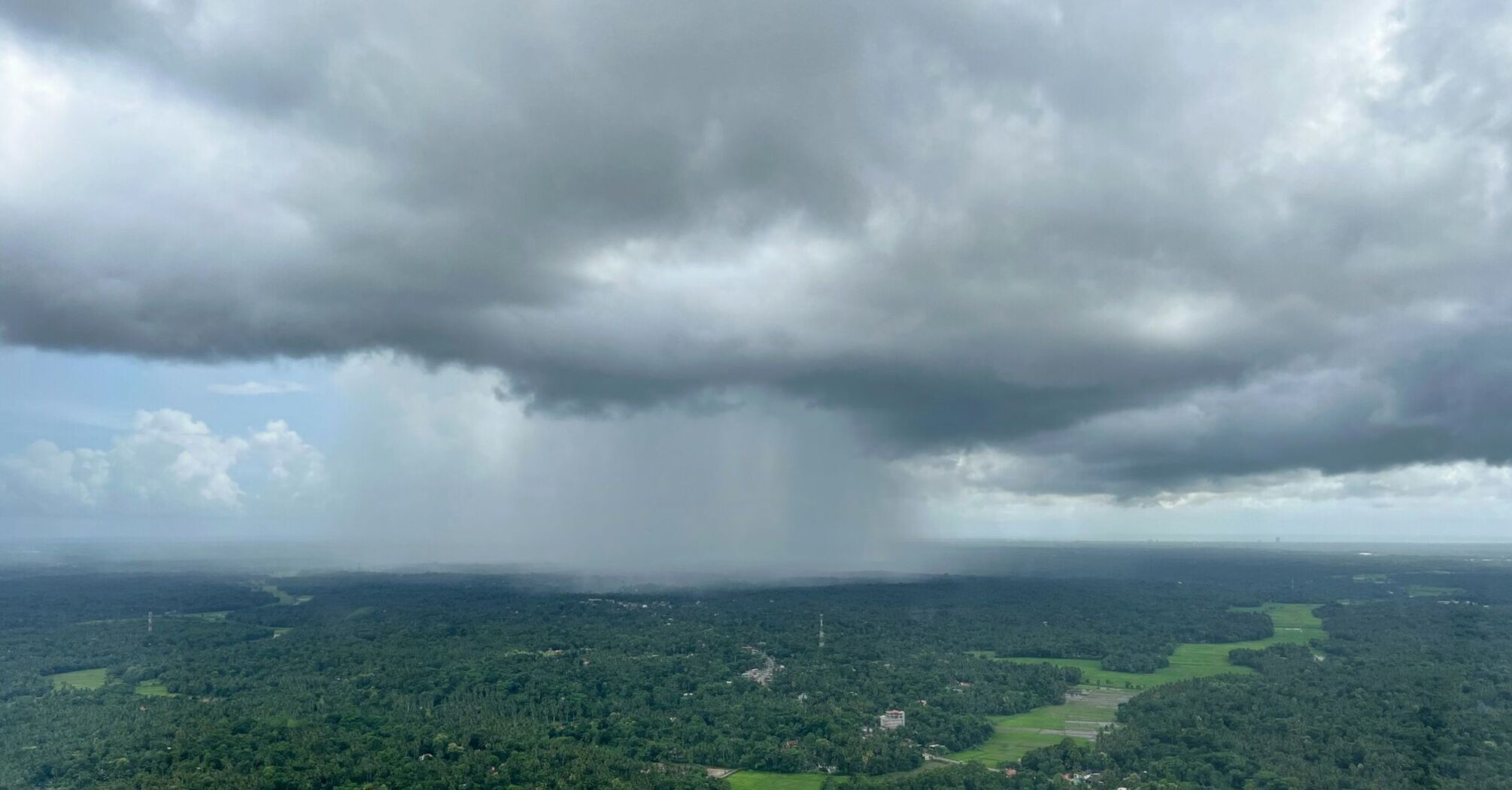 Dark storm clouds hovering over a green landscape, indicating approaching heavy rainfall