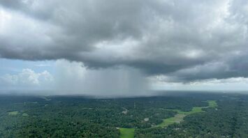 Dark storm clouds hovering over a green landscape, indicating approaching heavy rainfall