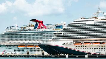 Two large cruise ships docked at a port under a partly cloudy sky