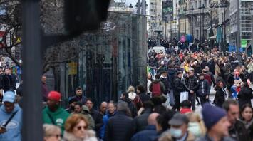 A busy city street with a crowd of people walking, a green traffic light in the foreground, and historical architecture in the background