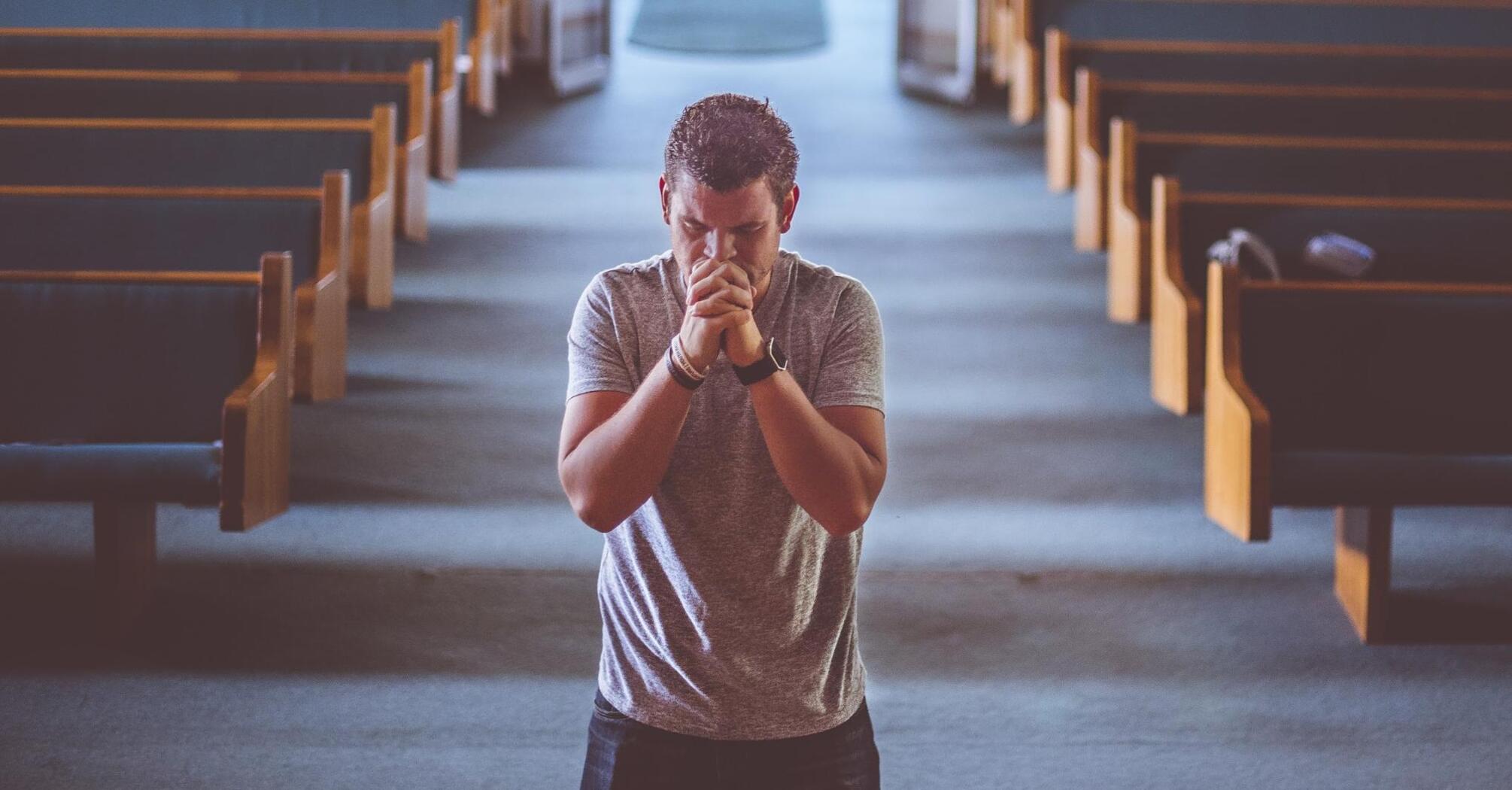 Man praying solemnly in a church aisle