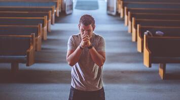 Man praying solemnly in a church aisle