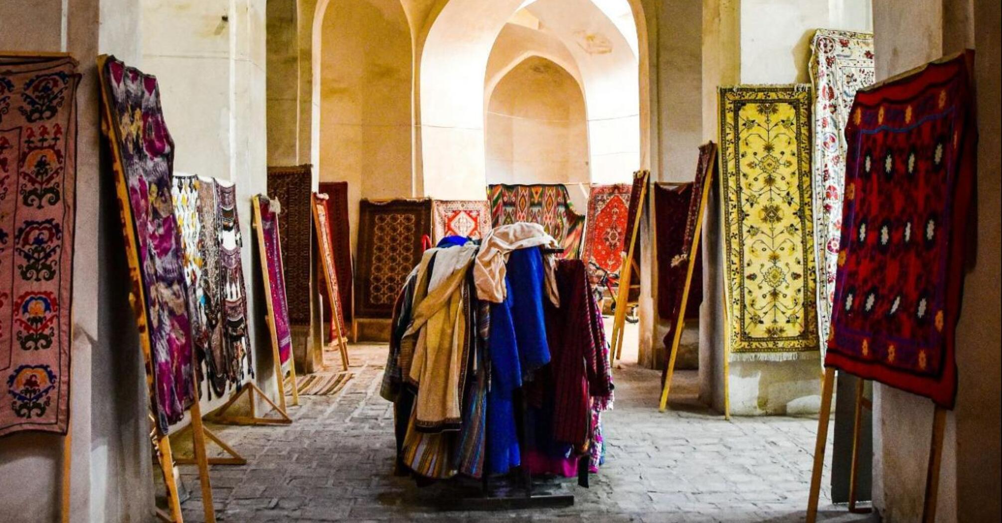 A traditional market stall displaying vibrant textiles and rugs inside an arched historical building