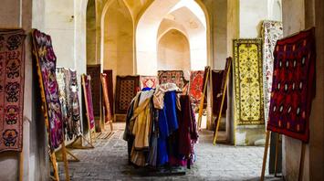 A traditional market stall displaying vibrant textiles and rugs inside an arched historical building