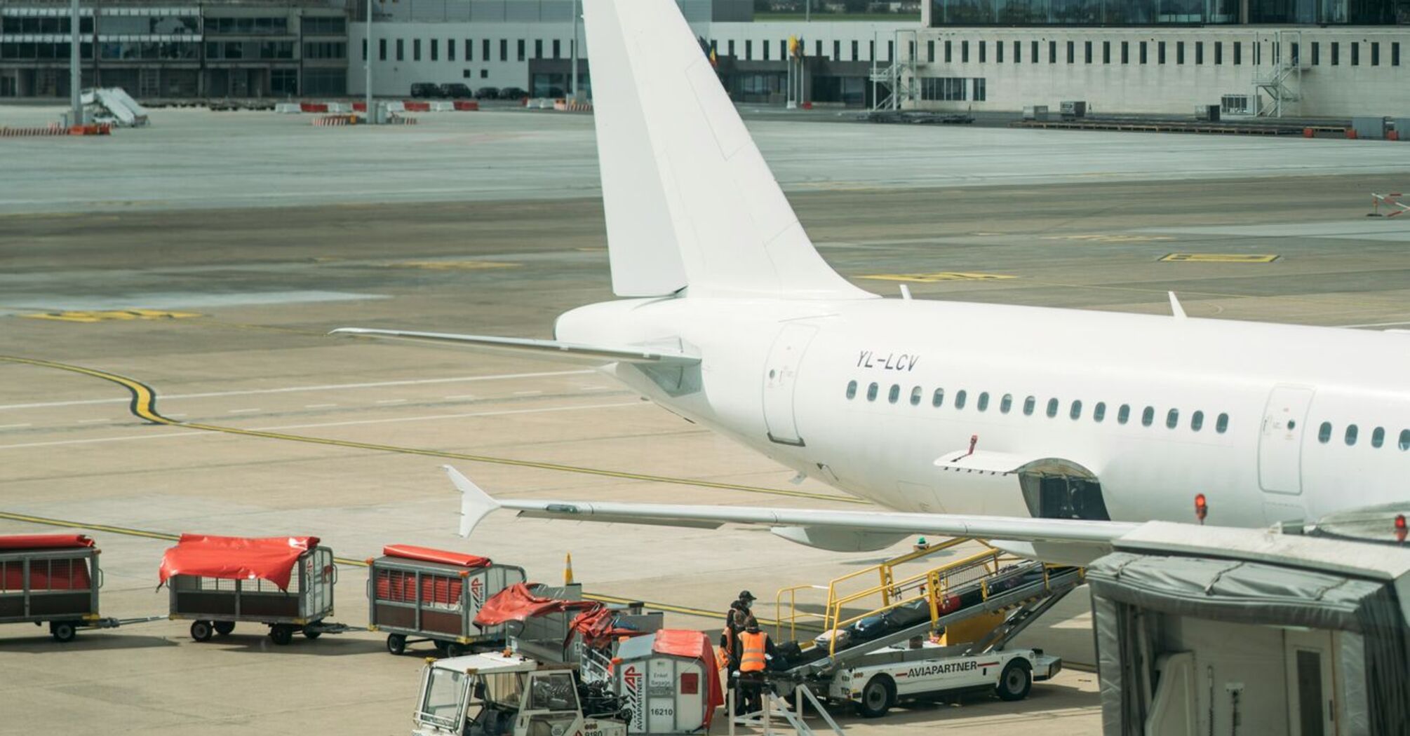 A white airplane parked on the tarmac at a Brussels airport, with airport ground staff working around the aircraft, and overcast skies in the background