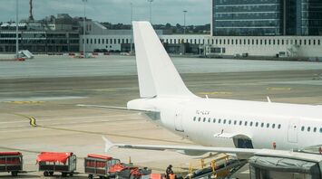 A white airplane parked on the tarmac at a Brussels airport, with airport ground staff working around the aircraft, and overcast skies in the background