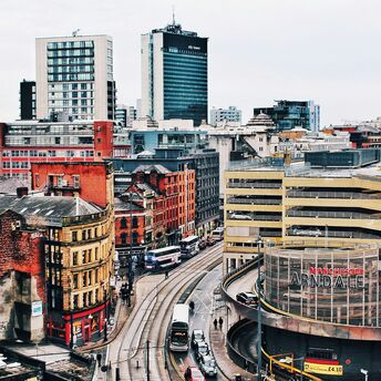 A view of central Manchester, showing trams, historic buildings, and the Arndale shopping center
