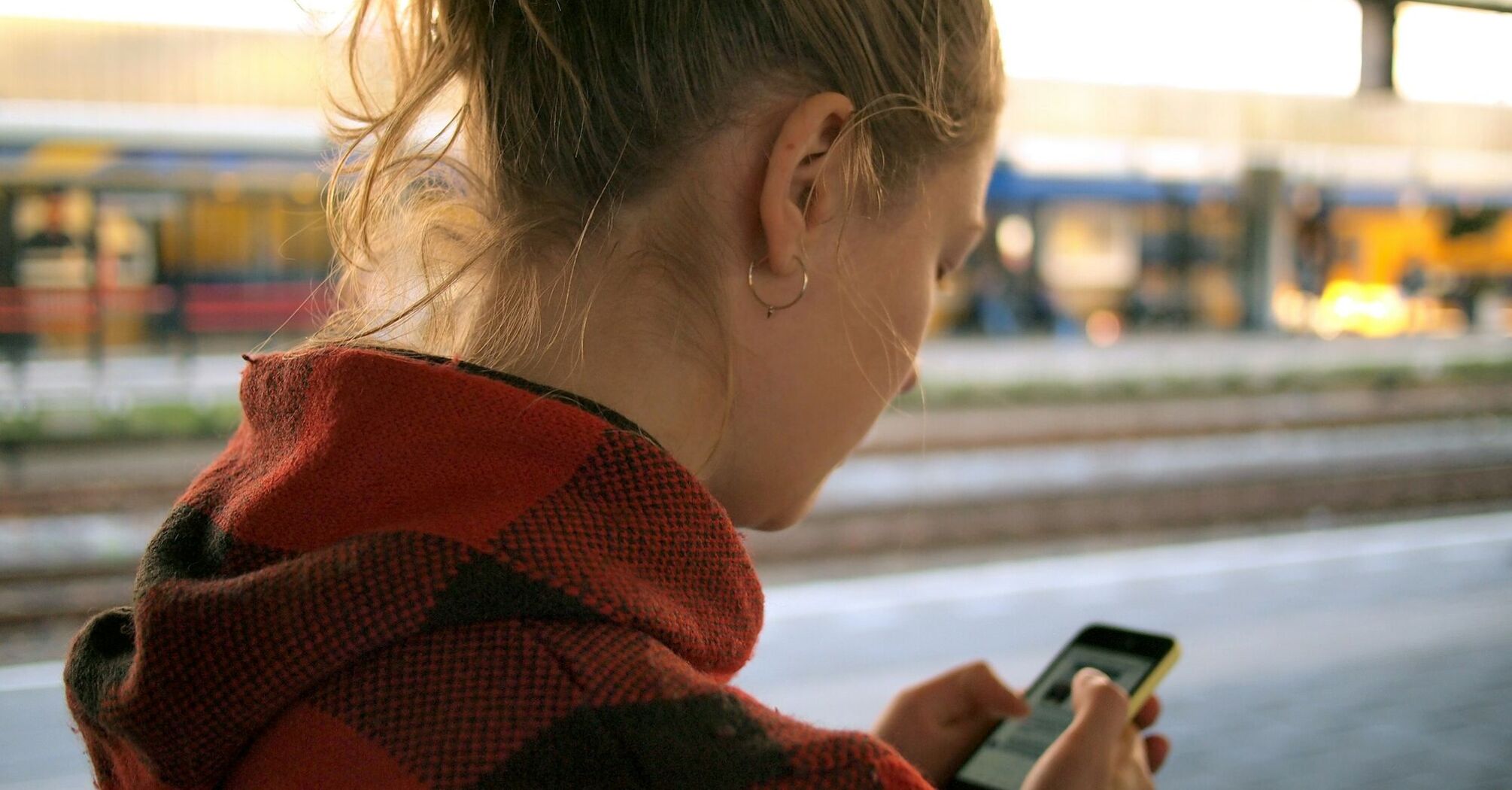 A woman checking her phone while waiting at a train station platform