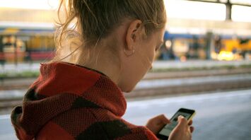 A woman checking her phone while waiting at a train station platform