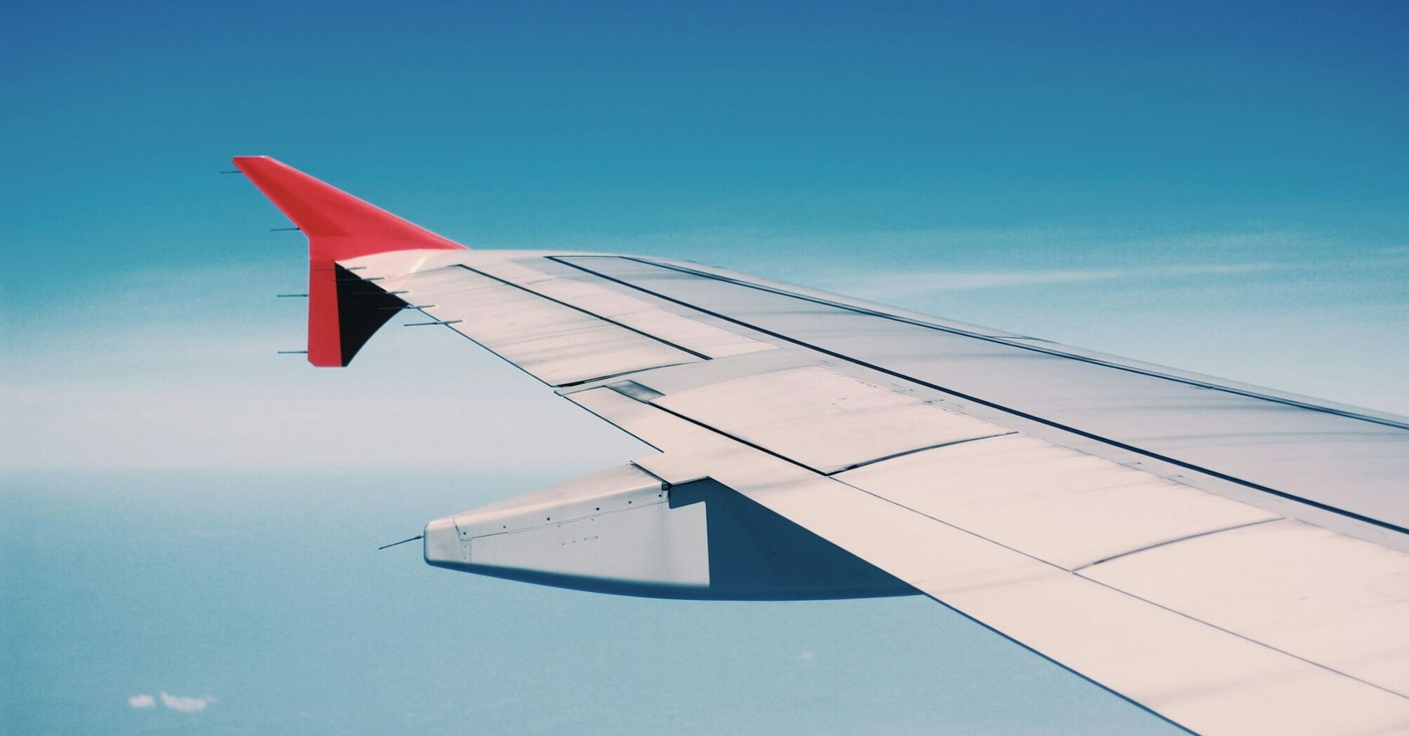 A view of an airplane wing against a clear blue sky during flight