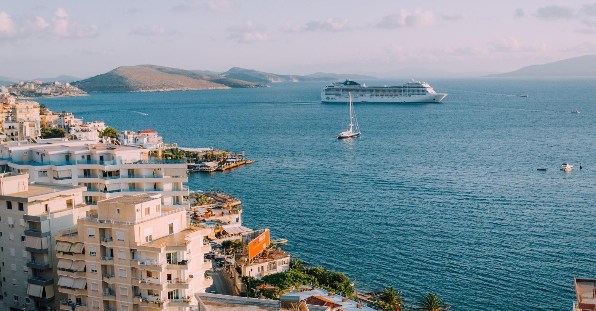 Aerial view of a coastal town with modern white buildings and a large cruise ship in the sea