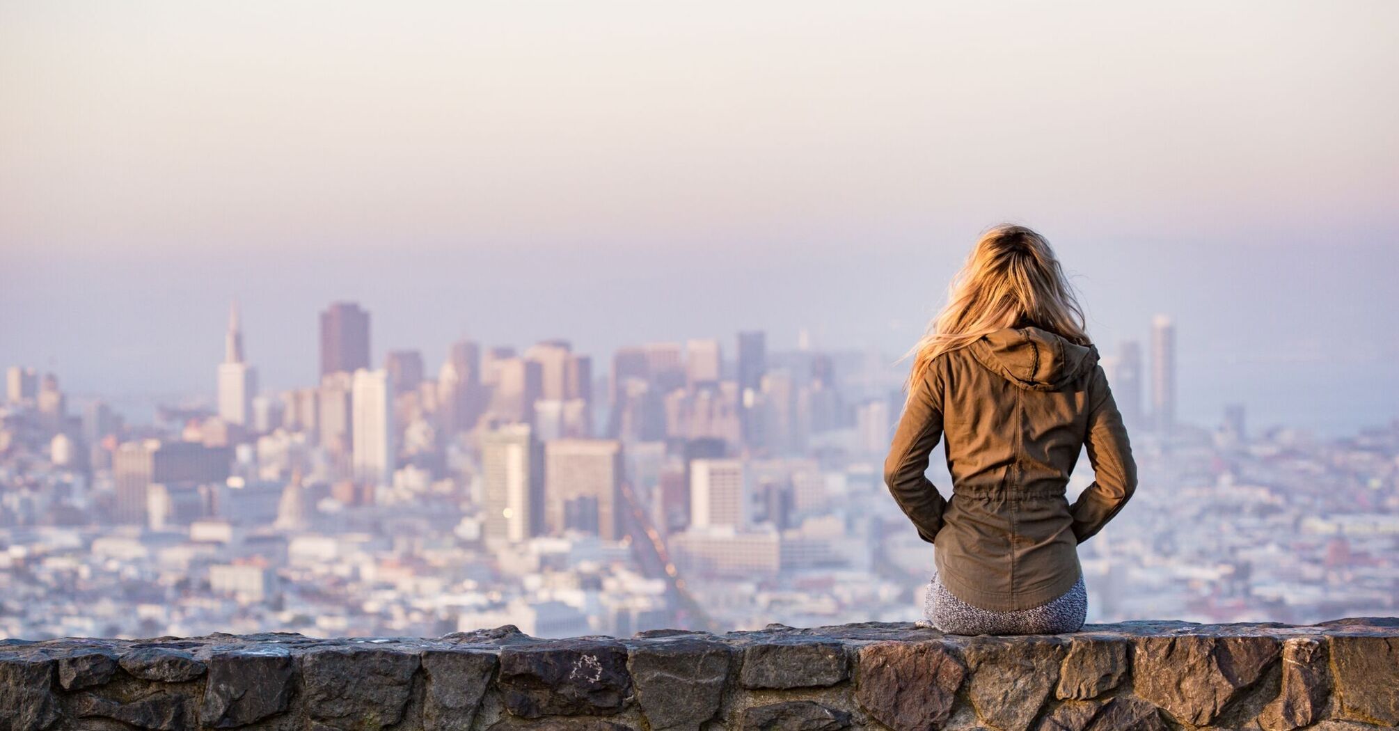 A woman sitting on a stone wall overlooking a city skyline